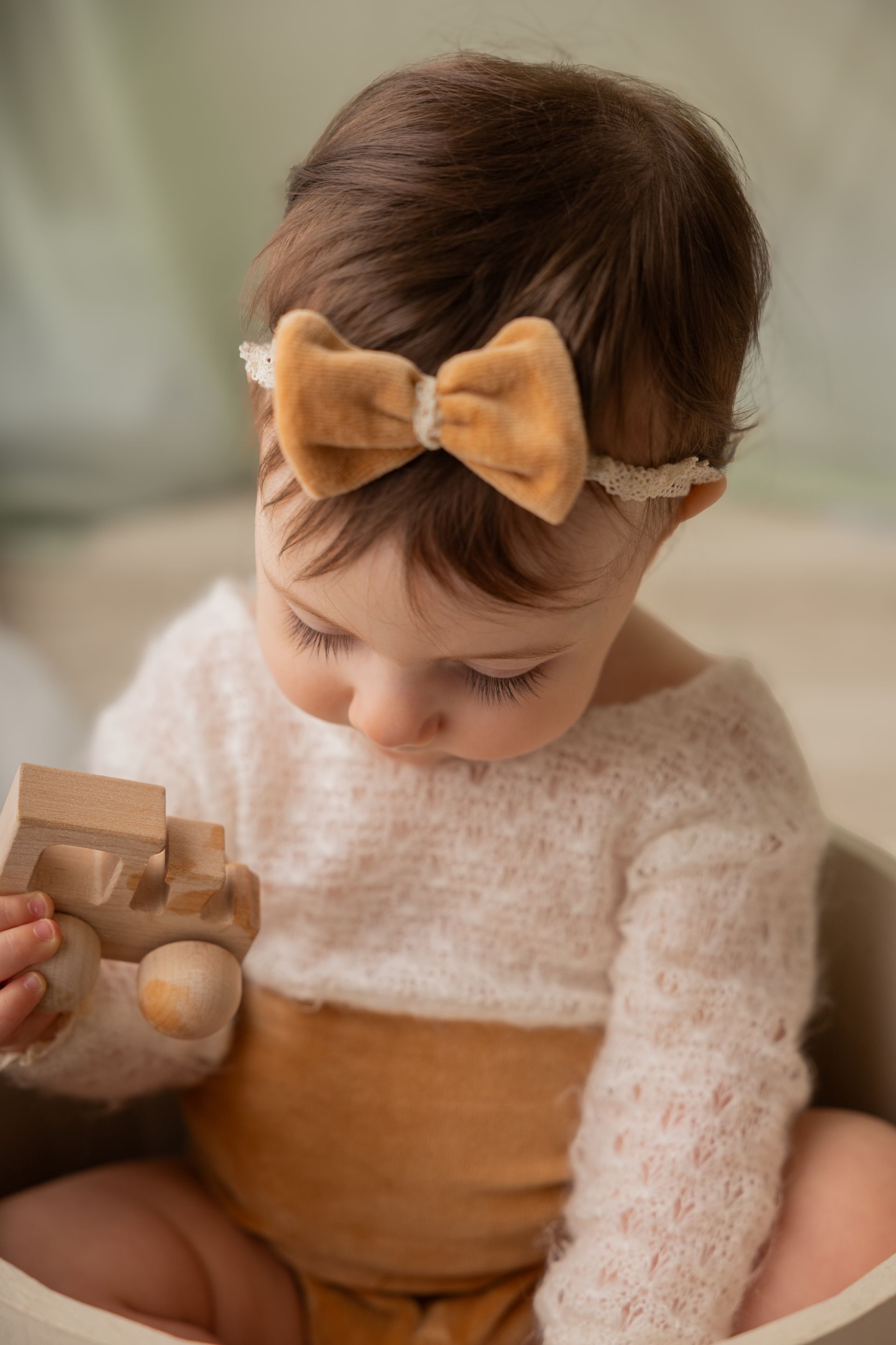 Bambina con maglia rosa cipria e fiocco di velluto osserva assorta una piccola macchinina di legno