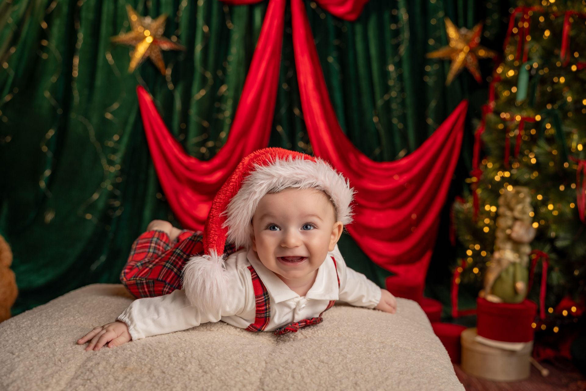 Bebè a pancia in giù con il cappellino di Babbo Natale, davanti al drappo rosso con il fiocco