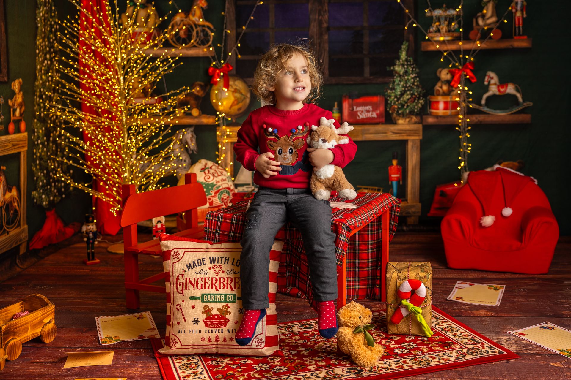 Bimba con il maglione della renna seduta su una scatola di pan di zenzero, accanto all'albero dorato