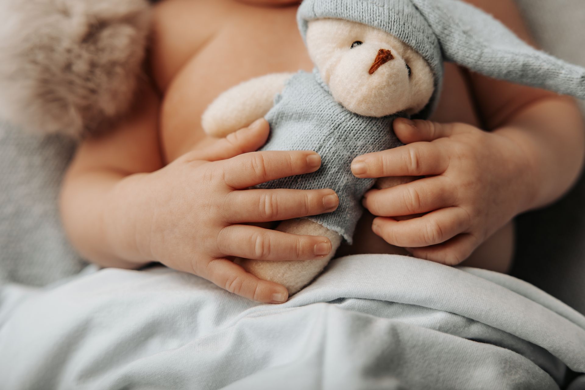 Manine di un neonato appoggiate su un orsetto azzurro di peluche sopra una copertina chiara