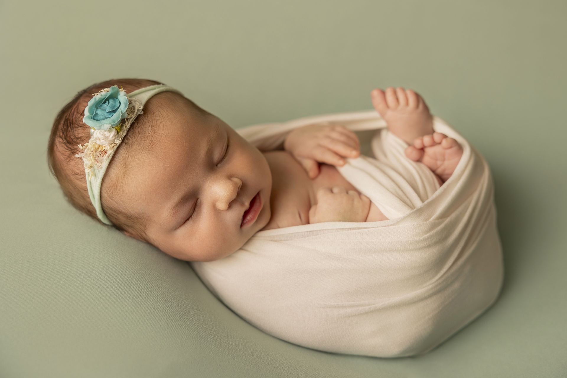 Neonata con fascia fiorita dorme fasciata di bianco su un caldo sfondo verde salvia