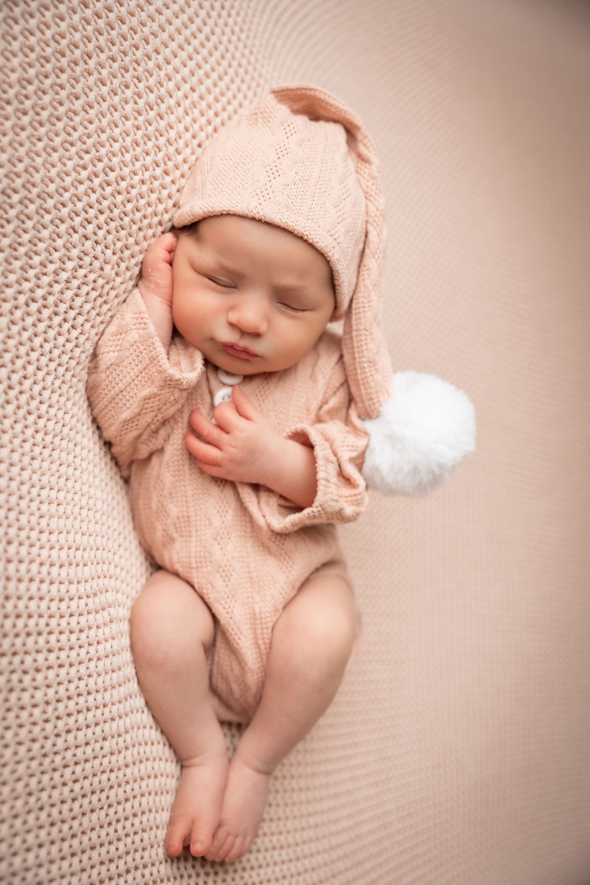 Bimbo con cappellino rosa dal pon pon bianco dorme disteso su una morbida coperta rosa