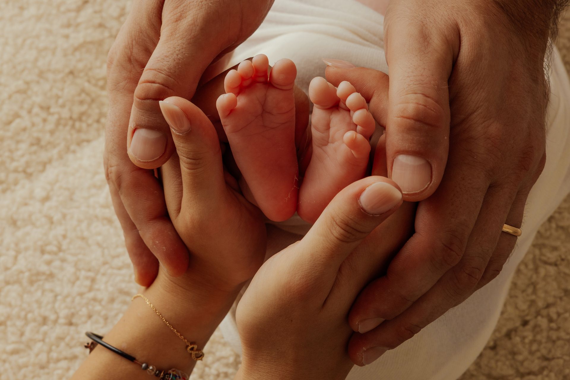 Piedini di un neonato racchiusi nelle mani intrecciate di mamma e papà su tappeto chiaro